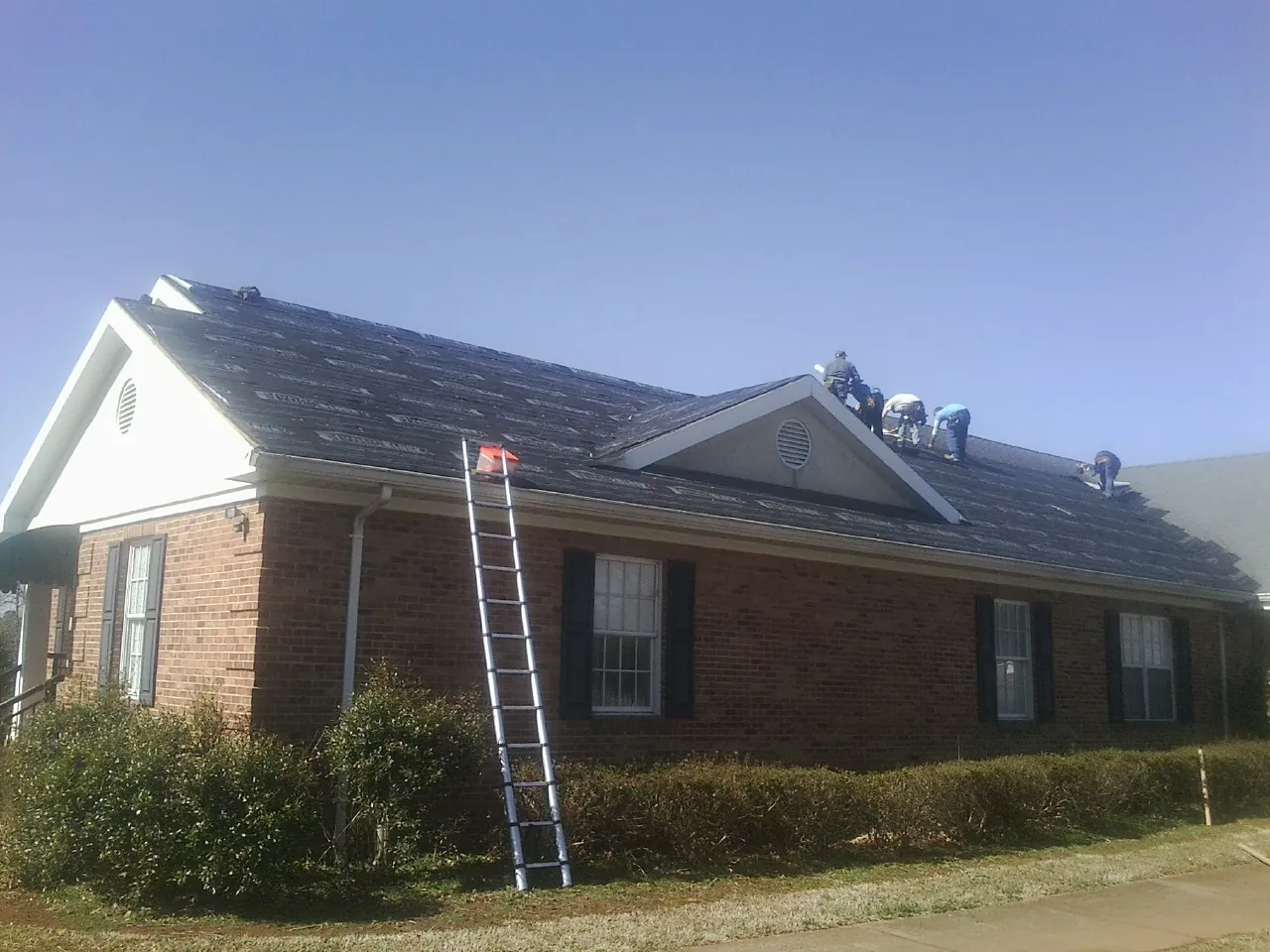 Crew tearing shingles off a brick ranch roof with a ladder set — Emergency Roof Repair work by our crew in Lithia