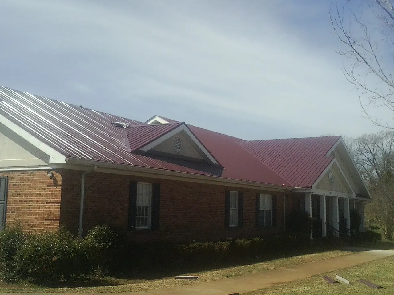 Red metal roof with gabled entries on a long brick building, from a Hail Damage Roof Repair job in Lithia