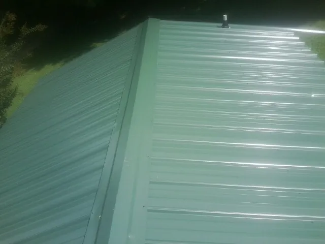 New green metal panels meeting at the ridge of a roof — Flat Roof Repair work by our crew in Lithia