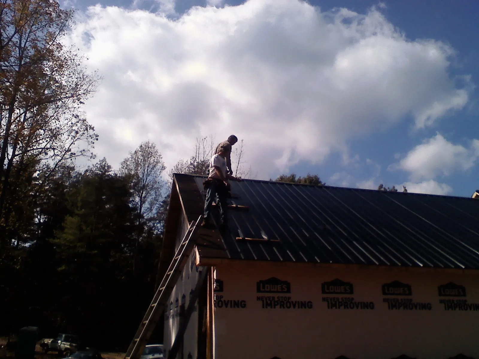 Roofer fastening dark metal panels high against a cloudy sky, from a Roof Inspection job in Lithia
